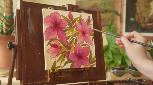 Pink flower painting on an easel, brush in hand
